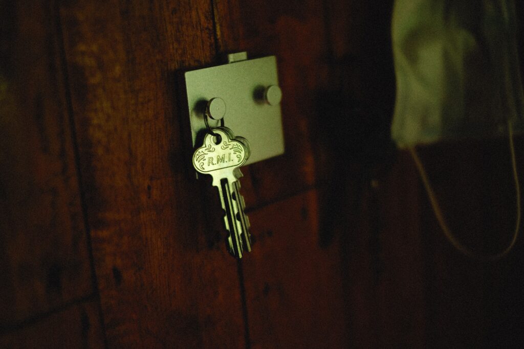 A close-up of a metallic key labeled 'R.M.I.' on a rustic wooden wall hook.