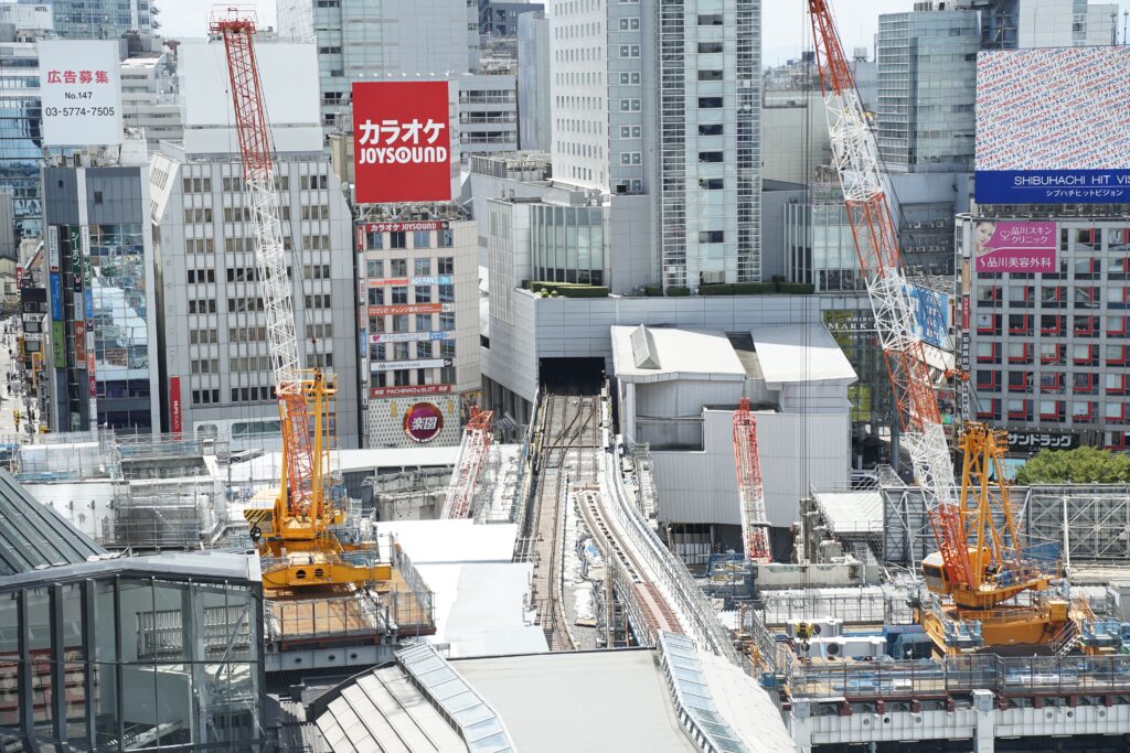 【保存版】無人インドアゴルフ開業ロードマップ!準備からオープンまでの全5ステップ Aerial view of construction cranes in Shibuya, Tokyo with skyscrapers.