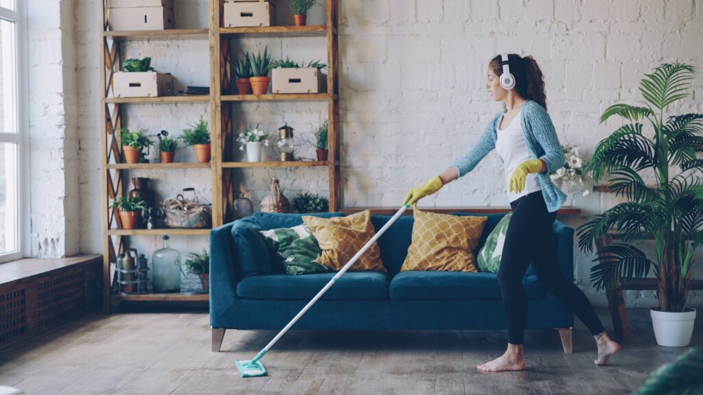 Woman wearing headphones and gloves while mopping a stylish indoor living room.
